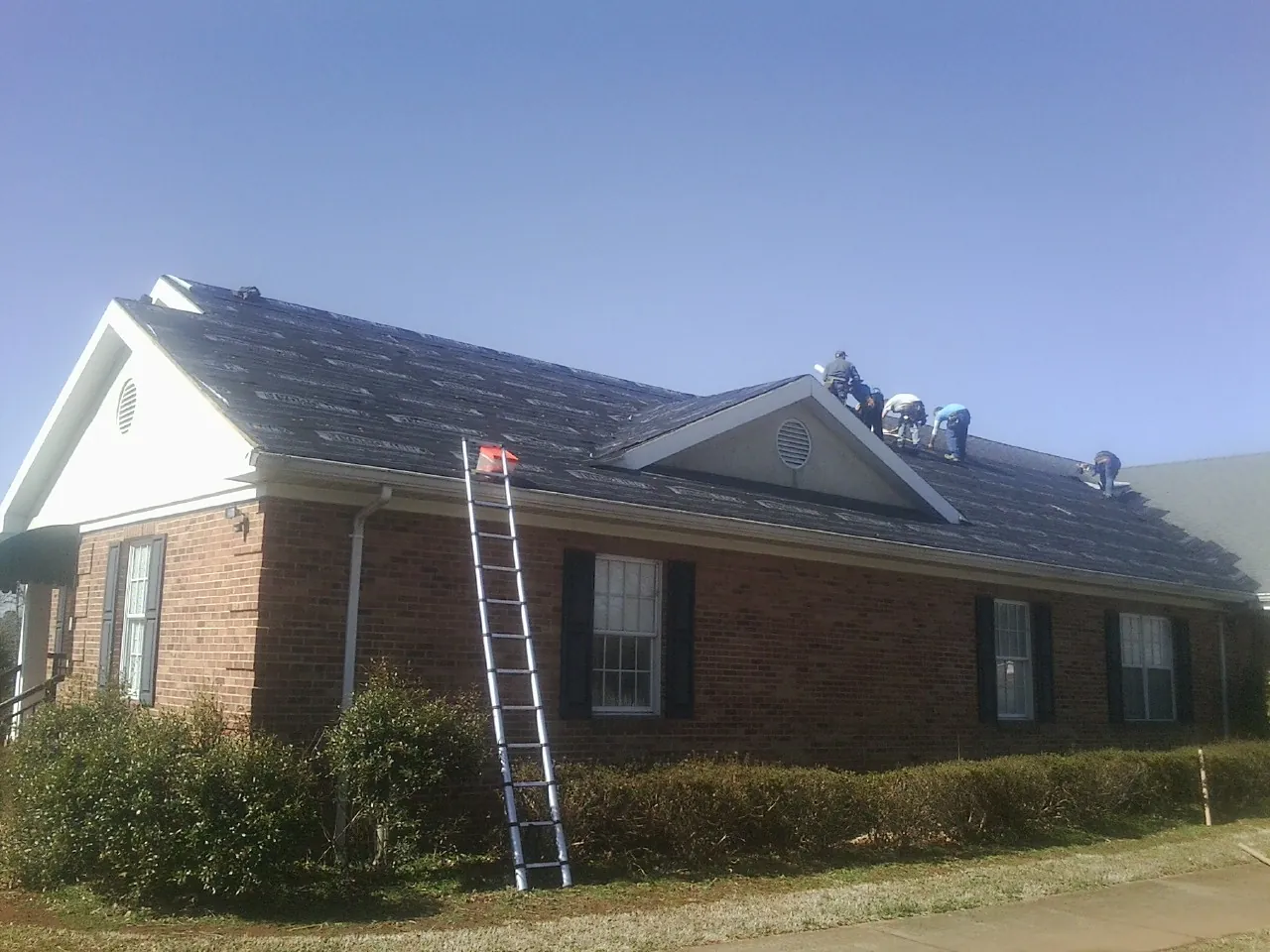 Crew tearing shingles off a brick ranch roof with a ladder set — Emergency Roof Repair work by our crew in Jeannette