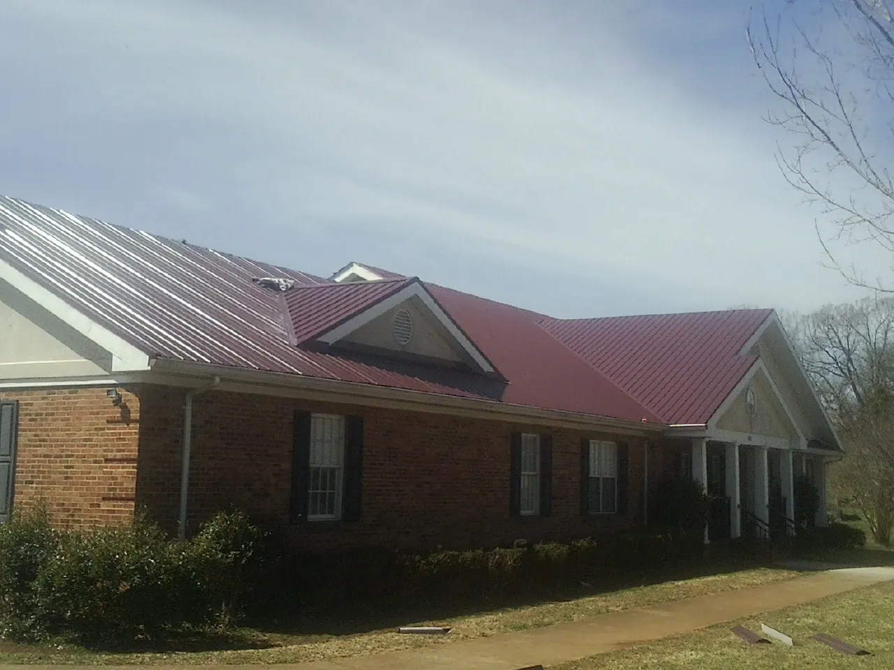 Red metal roof with gabled entries on a long brick building, from a Hail Damage Roof Repair job in Jeannette