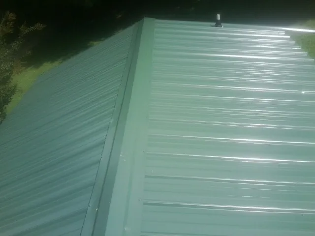 New green metal panels meeting at the ridge of a roof — Flat Roof Repair work by our crew in Jeannette