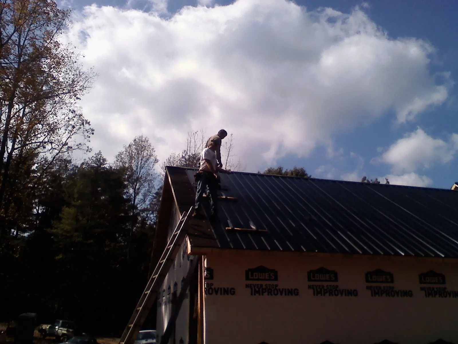 Roofer fastening dark metal panels high against a cloudy sky, from a Roof Inspection job in Jeannette