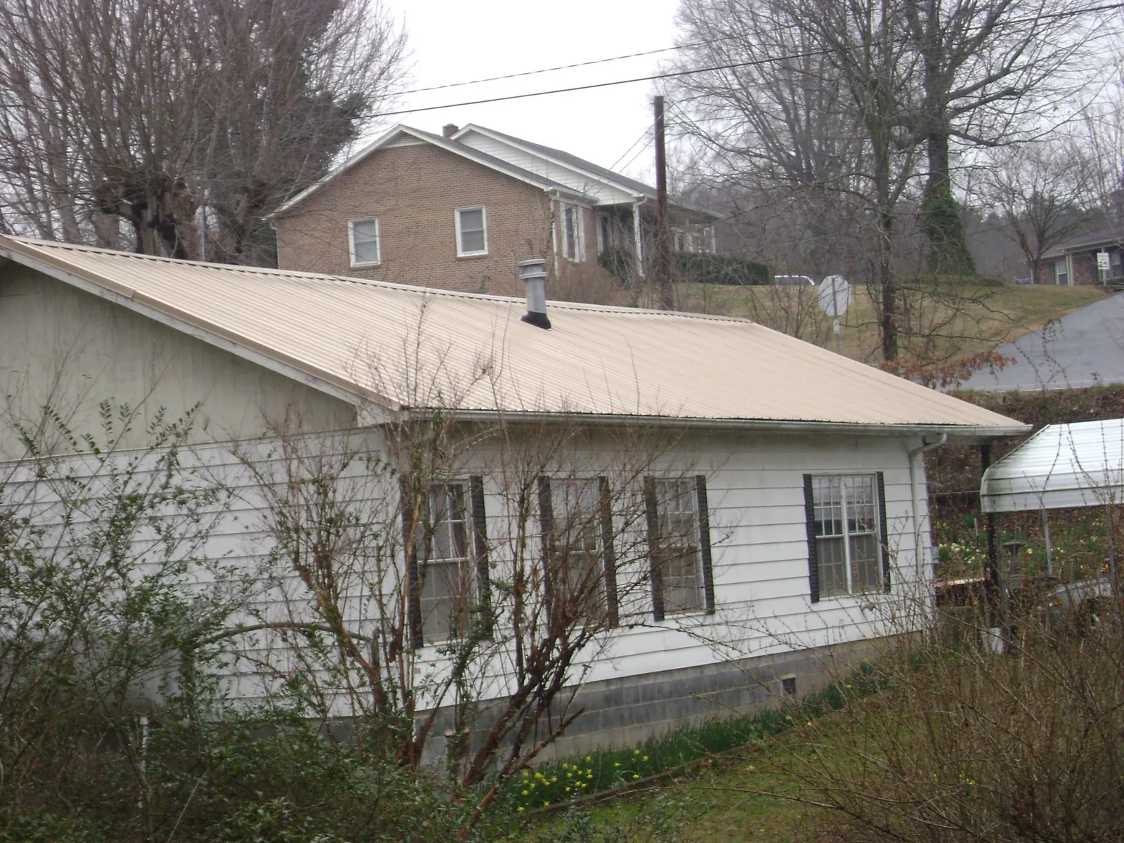 Tan metal roof on a white sided house set into a hillside — Commercial Roofing by Roofing Brothers in Jeannette
