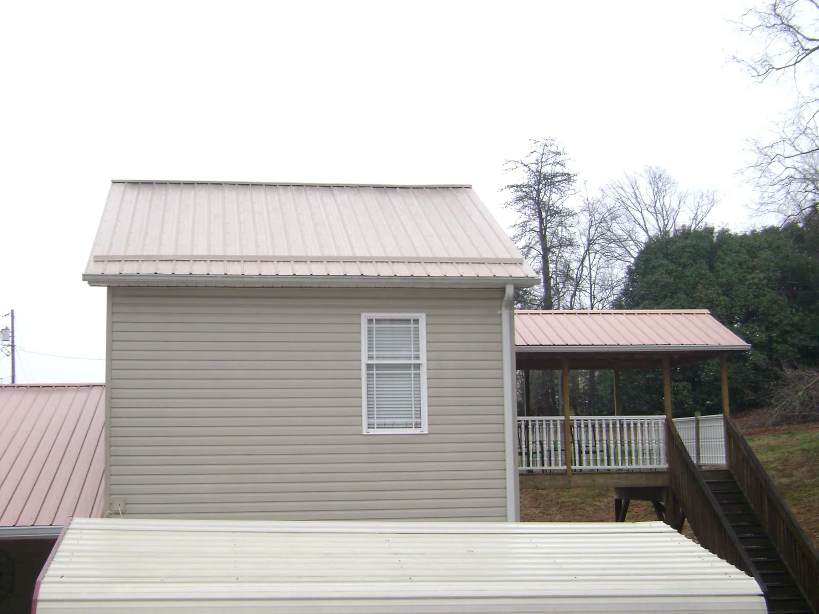 Tan metal roofs on a two story addition and attached porch, from a Roof Replacement job in Jeannette